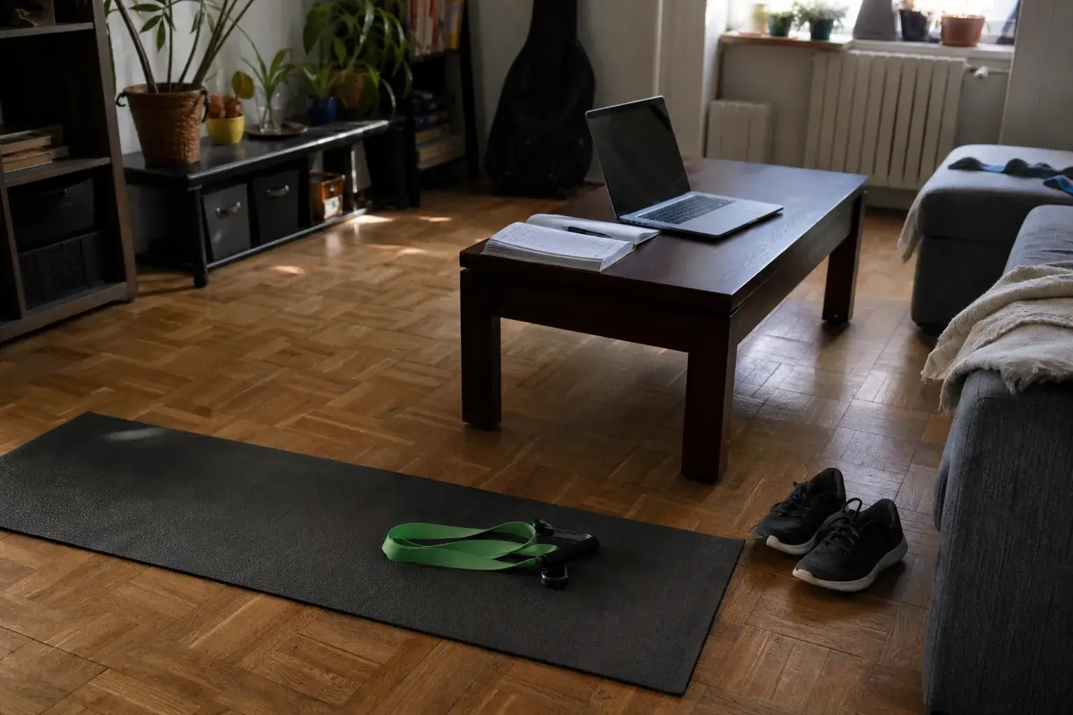 Coin de salon transformé en espace d’entraînement : tapis et élastique au sol, dossier de papiers et ordinateur portable sur la table basse
