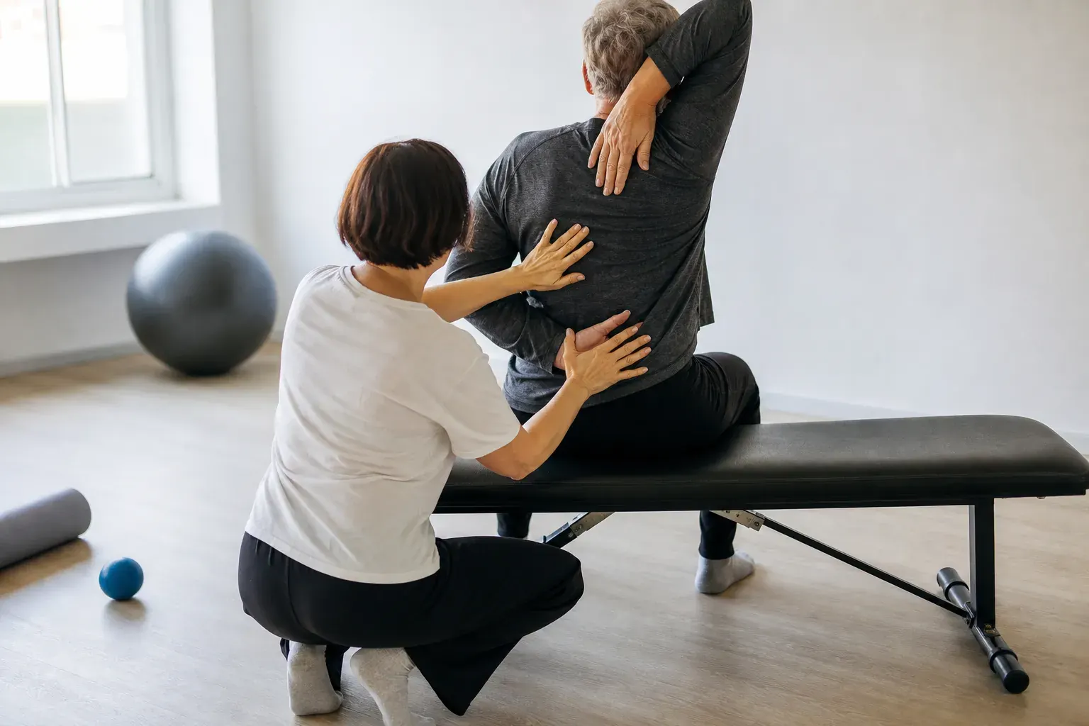 Séance de mobilité douce d’épaules, personne d’âge mûr assise sur un banc bas, encadrant accroupi à sa hauteur