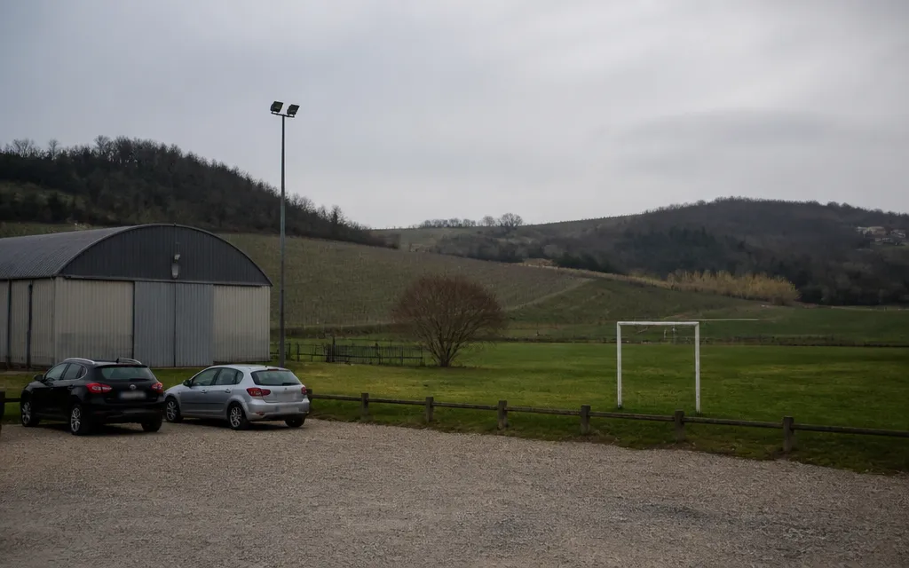 Petite salle des sports et terrain herbeux en périphérie de l’aire lyonnaise, vignes et collines boisées à l’arrière