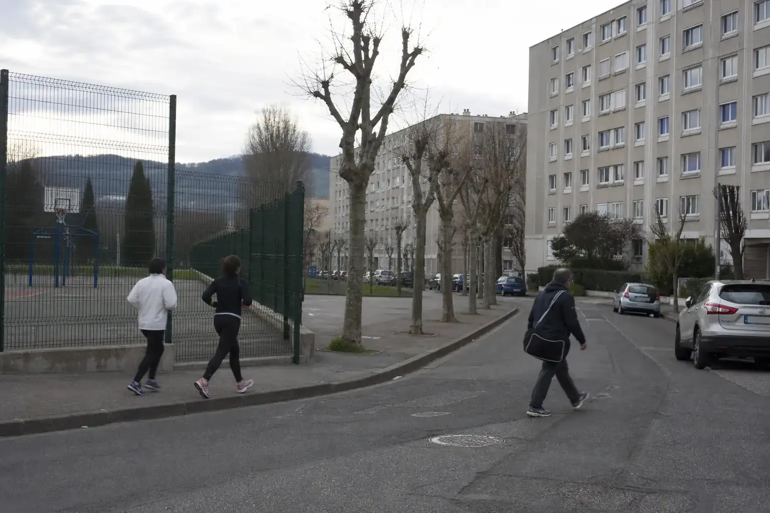Rue ordinaire d’une commune de l’agglomération lyonnaise, immeubles des années 1970 et city-stade en plein air en bord de trottoir